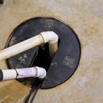 PVC plumbing pipes extending into a gray circular hole in a concrete surface for drainage by Quahog Plumbing.