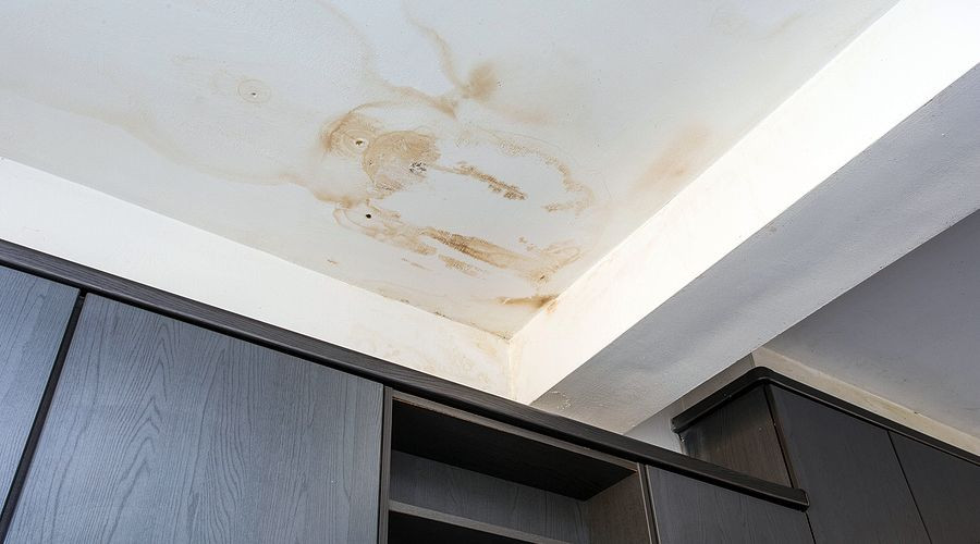 Ceiling with water damage and peeling paint above dark cabinets, indicating plumbing issues. Quahog Plumbing services.