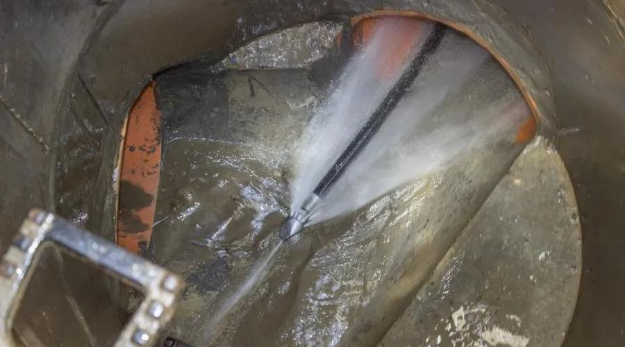 High-pressure water jetting tool cleaning gray pipe interior with strong water flow; Quahog Plumbing services.