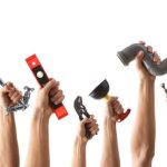 Hands holding a wrench, level, sander, and funnel, showcasing tools for Quahog Plumbing services and DIY projects.