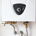 A white wall-mounted electric water heater with brass plumbing connections.