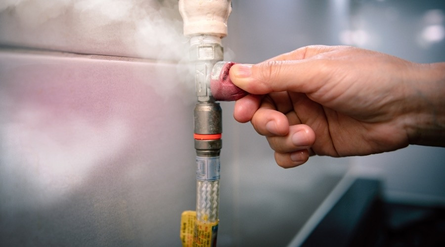 Hand turning a gas valve on a pipe, with steam visible, illustrating gas leak safety and plumbing services.