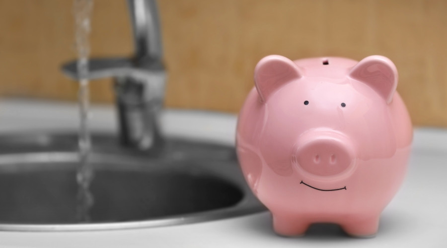 Piggy bank next to a kitchen sink with running water, symbolizing saving money on water bills and promoting water conservation habits.