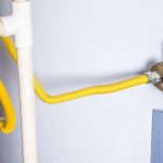 Gas water heater connection with yellow flexible gas line and plumbing fixtures, relevant to water heater installation services by Quahog Plumbing.