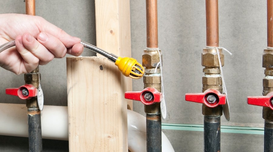 Hand adjusting a yellow valve on plumbing pipes, showcasing plumbing fixtures relevant to leak detection and repair.